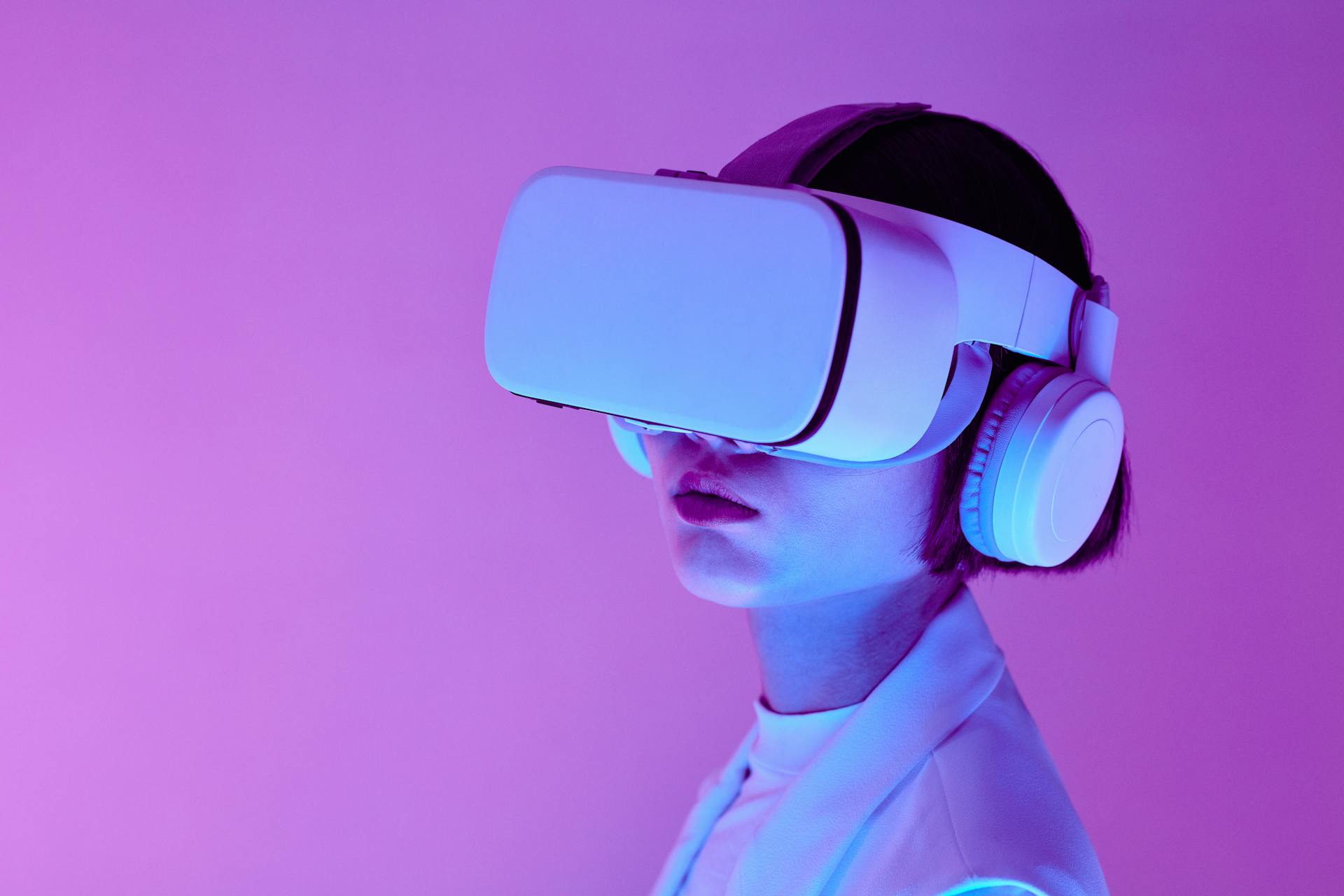 Trendsnip A TrendSnip user immersed in a virtual reality experience, wearing a VR headset and over-ear headphones, against a striking purple backdrop. Their light-colored outfit is bathed in soft, colorful lighting, evoking a futuristic and captivating ambiance.